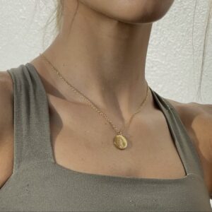 A woman wearing a necklace with a gold disc on it.