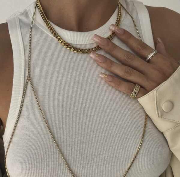A woman wearing gold jewelry and white nails.