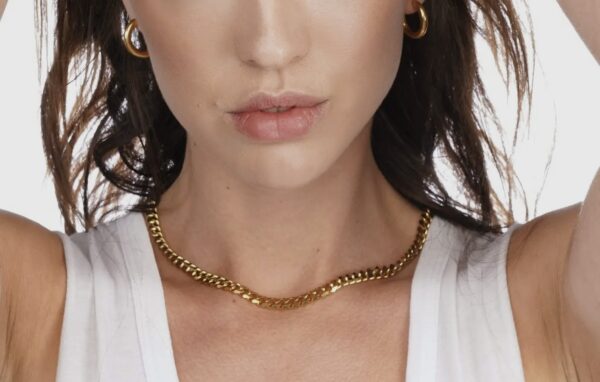 A woman wearing a gold chain necklace and earrings.